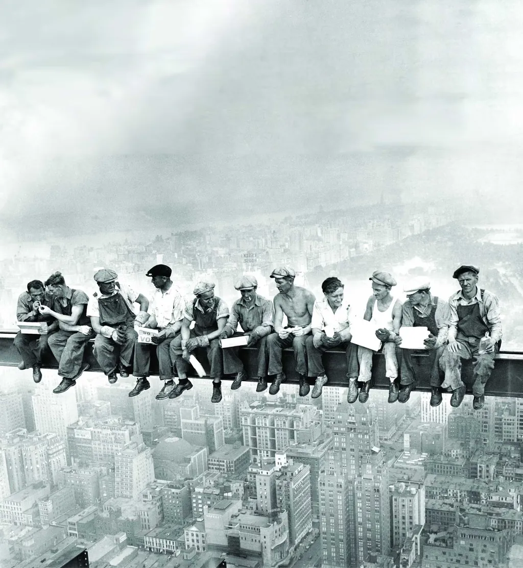 Eleven ironworkers eating lunch seated along a steel girder high above Manhattan, photographed during the construction of Rockefeller Center in 1932.